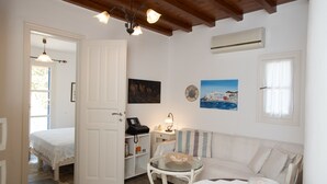 A cozy room with a bed, a small table with a lamp, a sofa, and a painting on the wall. - Villa Anemoessa Olive Green with Pool (Mykonos)