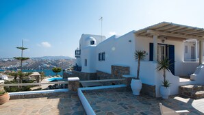 A white building with a stone terrace, a pool, and a view of the sea. - Villa Anemoessa Olive Green with Pool (Mykonos)