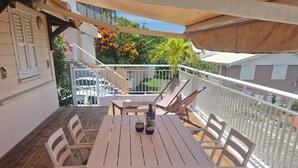 En träveranda med ett bord och några stolar, en flaska och ett glas.