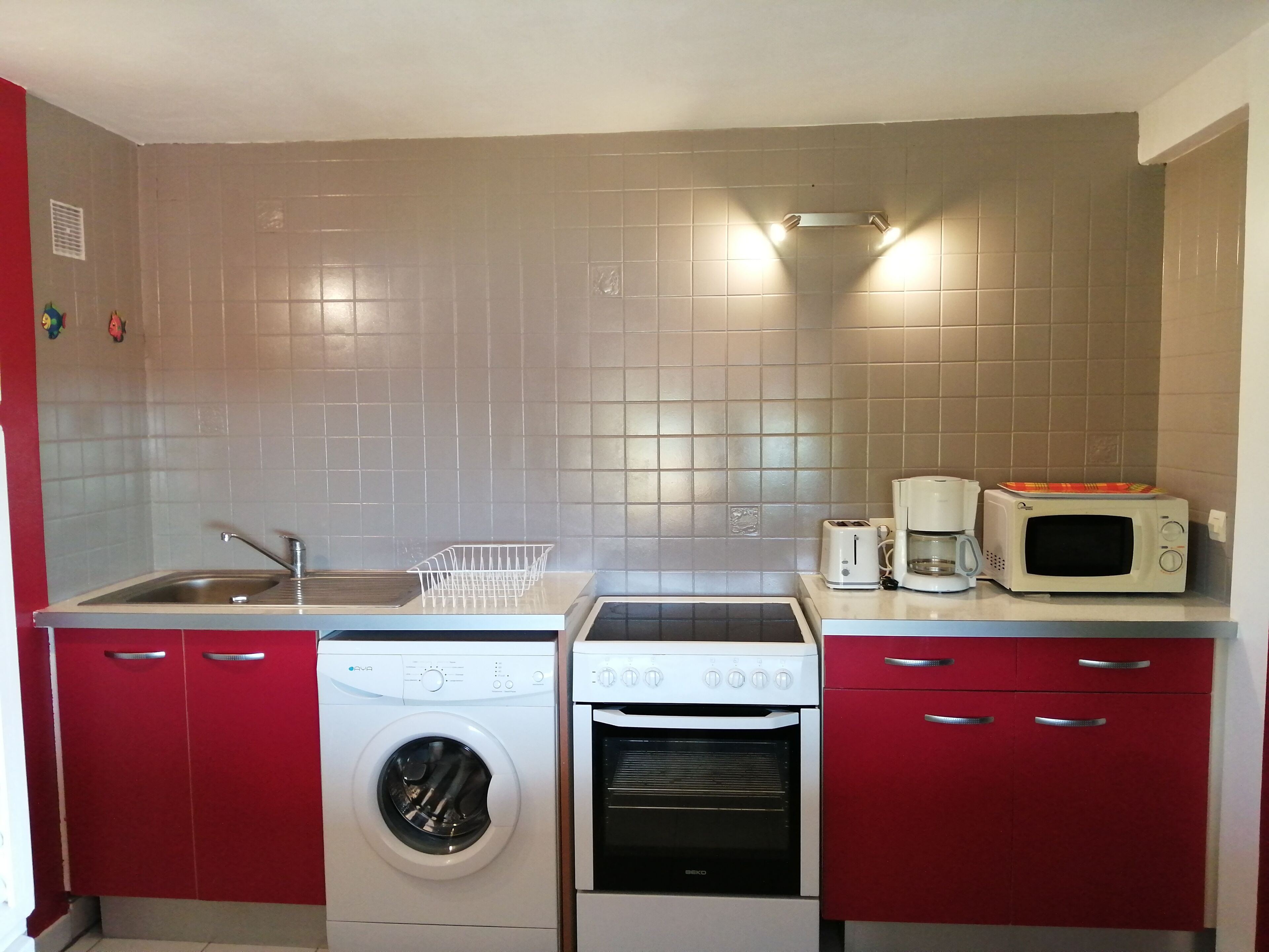 A compact kitchen with a washing machine, oven, microwave, and a sink.
