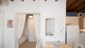 A small, clean room with a wooden table and chairs, a white door, and a window with a decorative mirror. - Villa Anemoessa Sky Blue with Pool (Mykonos)