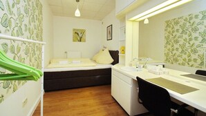 Une chambre d’hôtel de taille réduite, comprenant un lit, un bureau avec une chaise, un lavabo et un miroir.