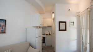 Een knus woongedeelte met een kitchenette, een bank en een ingelijst foto aan de muur.