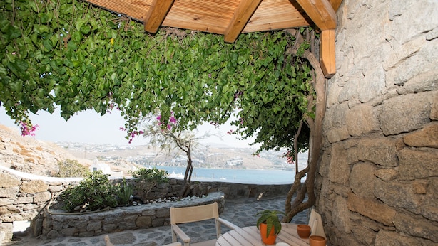 Een terras van natuursteen met een houten tafel en stoelen, een bloempot en uitzicht op de zee.