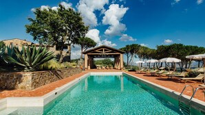 Une piscine d’un bleu éclatant, agrémentée d’un gazebo en bois au centre, entourée de chaises longues et de parasols.