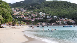 Una playa con casas en una colina, agua cristalina y gente nadando.