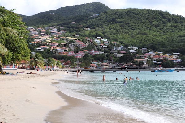 Une plage avec des maisons sur une colline, une eau cristalline et des gens qui se baignent.