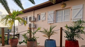 Terraza de madera con plantas en macetas y unidades de aire acondicionado instaladas en la pared de un edificio.