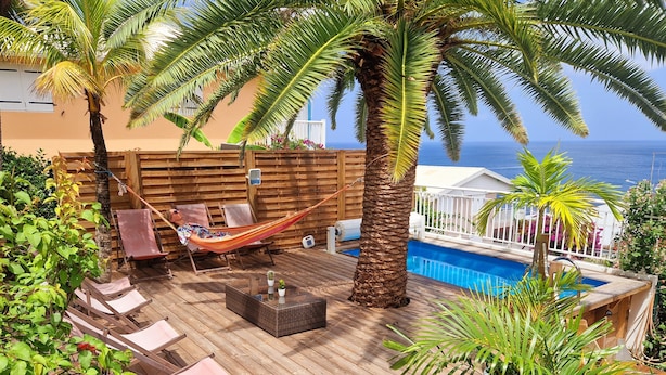 Una terraza de madera con piscina, sillas de descanso y una hamaca.