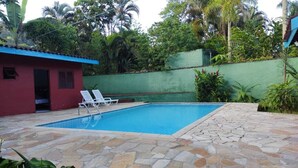 A swimming pool with stone tiles, a red building, and lush greenery. - Beautiful comfortable house (São Sebastião)