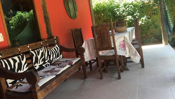 A wooden bench with zebra-patterned cushions, a table with a floral tablecloth, and a chair with a basket on it. - Beautiful comfortable house (São Sebastião)