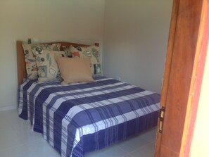 A bedroom with a bed, a headboard with patterned pillows, and a wooden door.