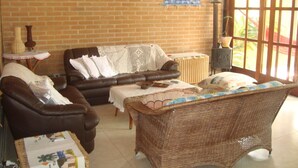 A cozy living room with a brown leather sofa, a wicker chair, and a small table with a vase. - Beautiful comfortable house (São Sebastião)
