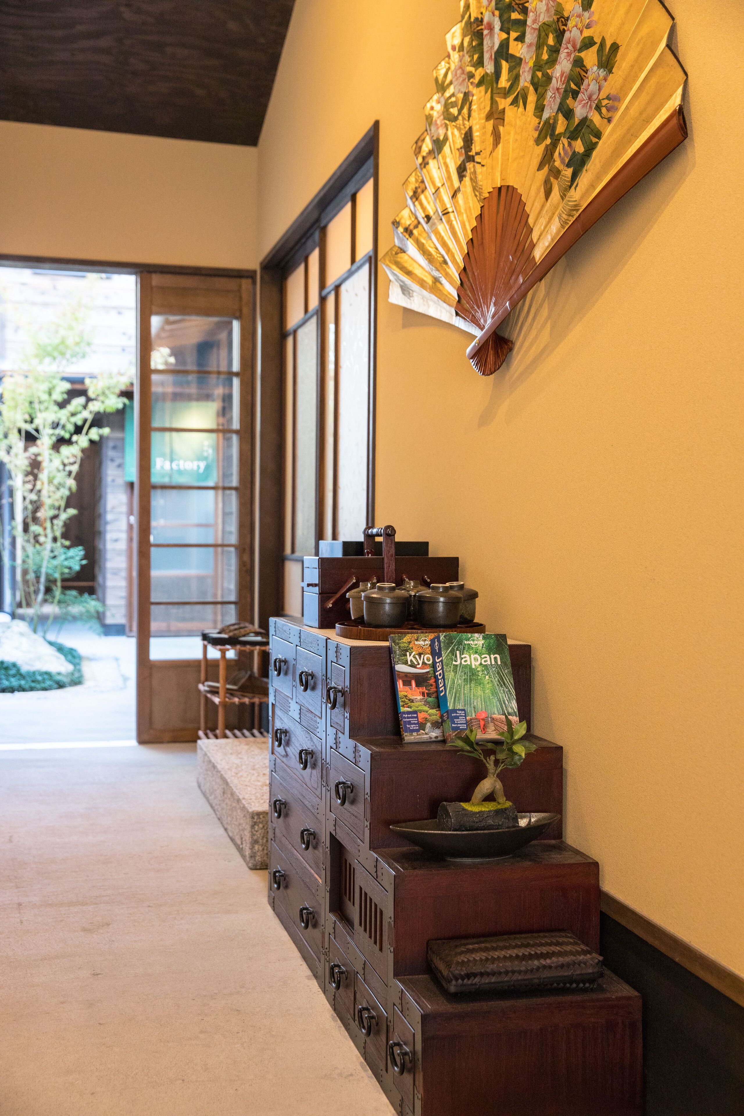 A traditional Japanese interior with a sliding door, a wooden cabinet with drawers, a fan, and a bonsai plant.