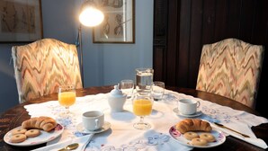A breakfast table set with croissants, juice, and coffee cups, surrounded by patterned chairs.