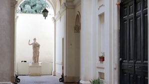 A corridor with a statue, columns, a door, and potted plants.