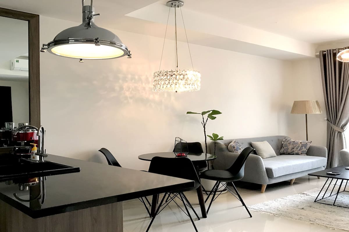 Un salon moderne comprenant un coin repas, un canapé gris, un lustre et un grand miroir.