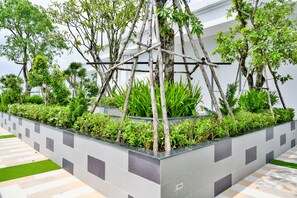 A modern outdoor area with a geometric tile pattern, a wooden trellis structure, and various green plants.