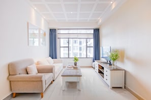 A modern living room with a sofa, coffee table, TV, and a view of buildings through large windows.
