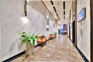 A modern hotel lobby with marble walls, wooden chairs, and potted plants.