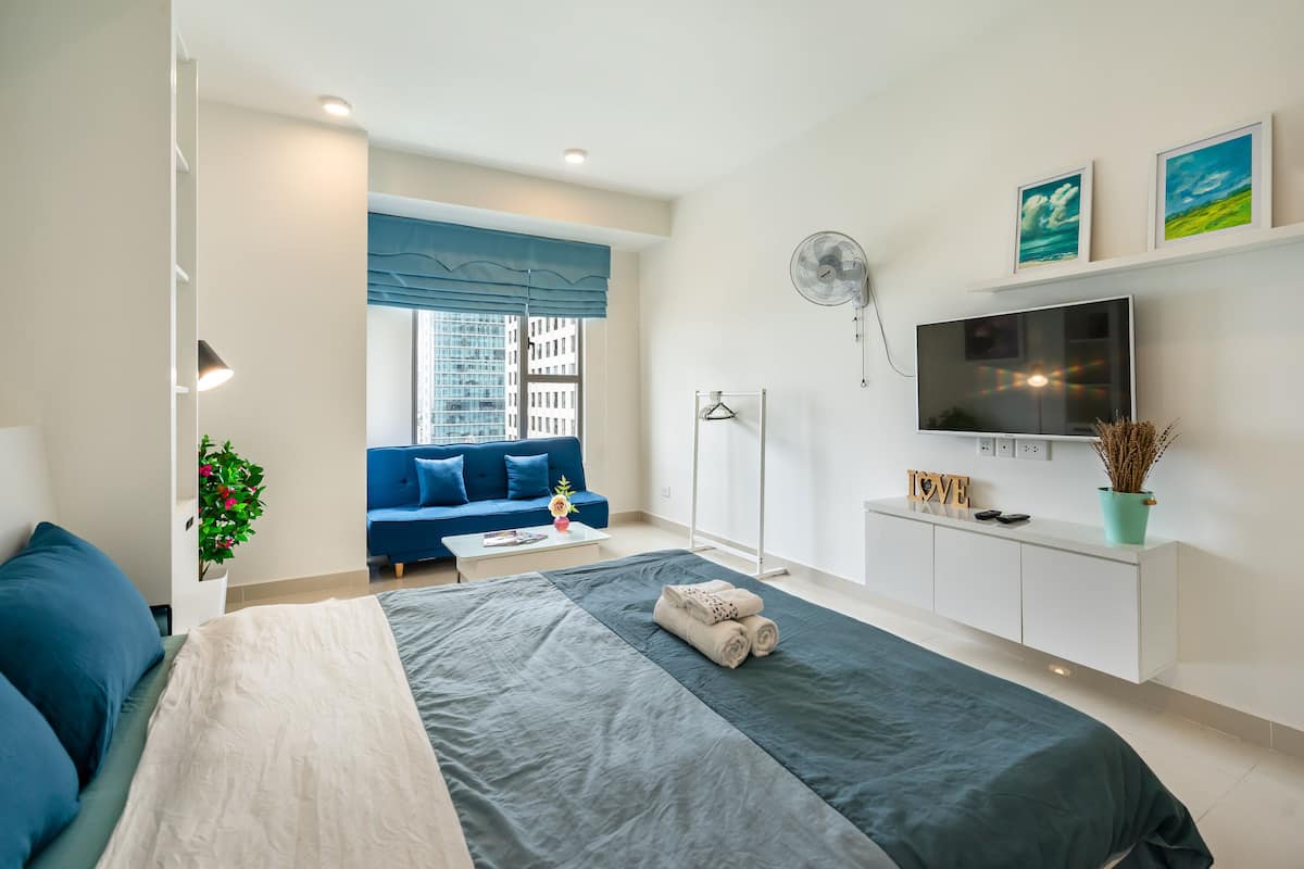 Une chambre moderne avec un lit, une télévision, un canapé et une fenêtre équipée de stores.