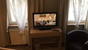 Ein Fernseher auf einem Holzständer in einem Zimmer mit Heizkörper, einem Sessel und durchsichtigen Vorhängen.