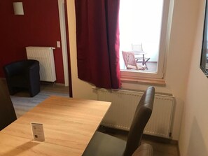 A room with a wooden table and a single chair, a radiator, and a window with red curtains.