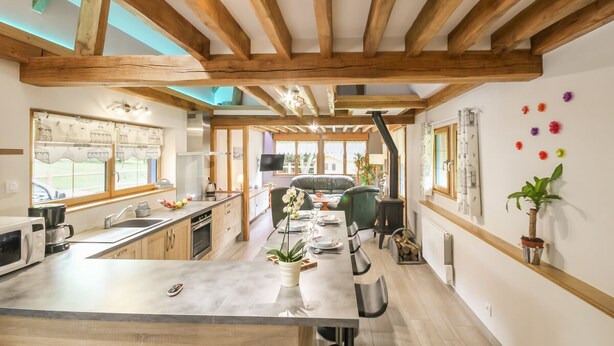 Una cocina moderna con vigas de madera, un comedor con mesa y sillas, y vistas al exterior.