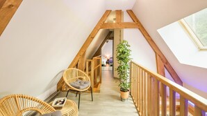 Una escalera de madera con vistas a un dormitorio. Hay sillones de mimbre y una planta en maceta.