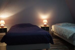Ein Schlafzimmer mit zwei Betten, jeweils mit einer Nachttischlampe. Das Zimmer hat eine schräge Decke und Holzdielen.