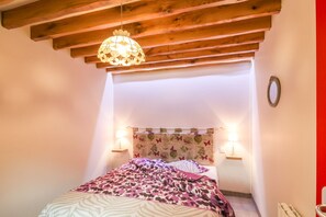 Une chambre avec un plafond en bois, un lit recouvert d’une couvre-lit à motifs, deux lampes de chevet et une horloge fixée au mur.