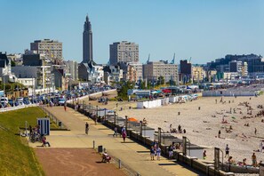 Ein Strand mit Menschen, einer Promenade und Gebäuden im Hintergrund.