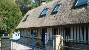 Una casa tradicional con techo de paja, fachada de madera, entrada con portón y un pequeño cobertizo adyacente.