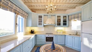 Une cuisine avec des meubles de couleur bleu clair, un îlot central, un lustre et une vue par la fenêtre.