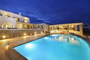 Un espace aménagé au bord de la piscine, avec des murs en pierre, des chaises longues et un espace extérieur bien éclairé.