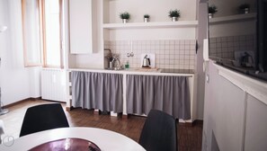 A modern kitchen with a white countertop, grey curtains, and a dining area with a table and chairs. - Italianway Easy - Corso Como 8 (Milano)