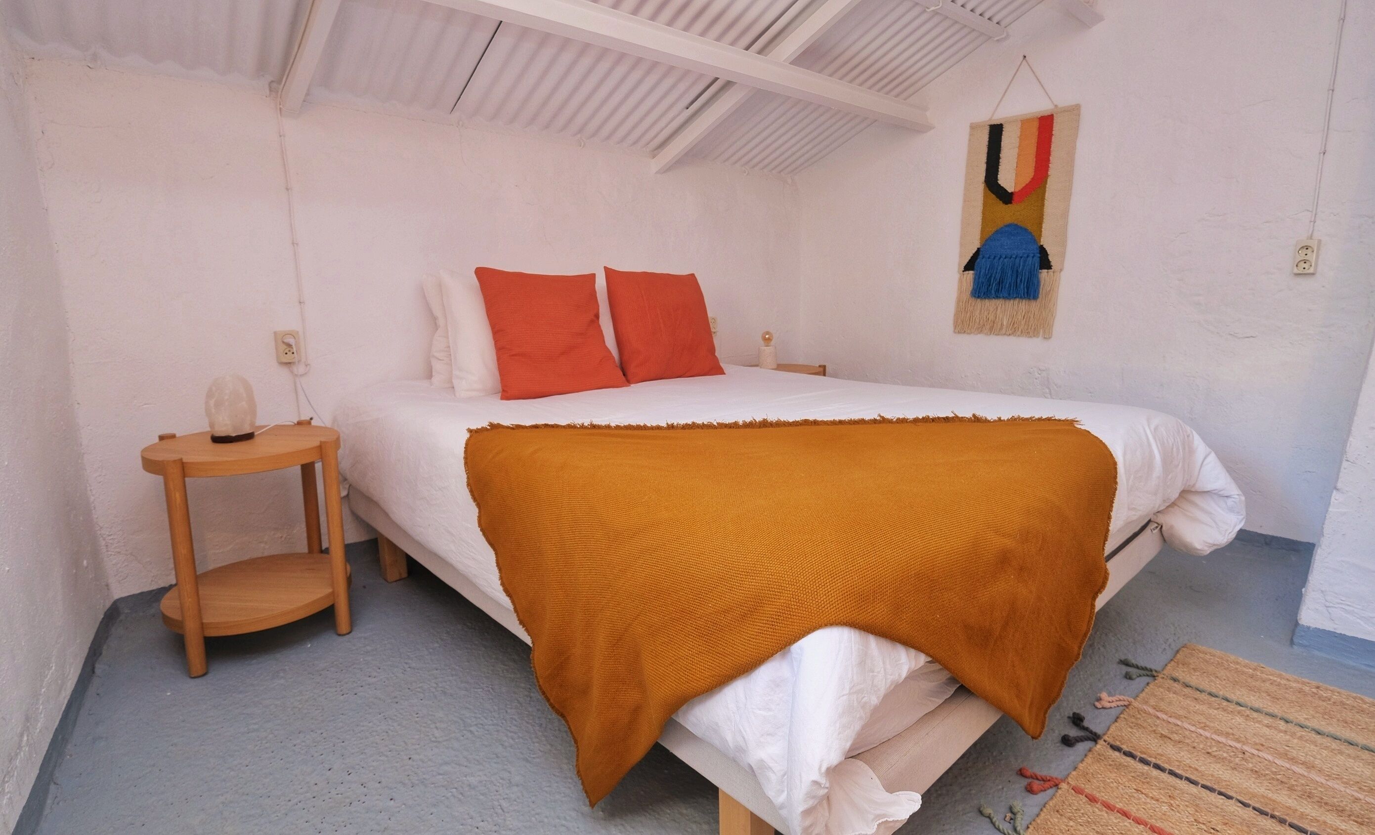 A bedroom with a bed, a bedside table, a wall hanging, and a rug.