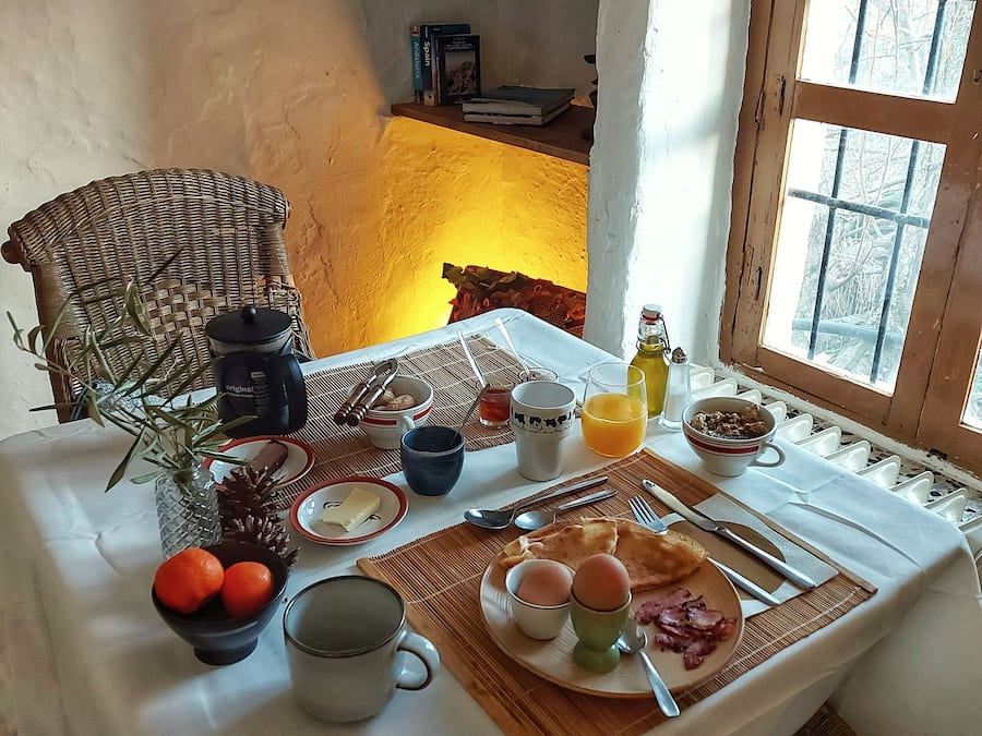 Una mesa con alimentos para el desayuno y una silla de mimbre.