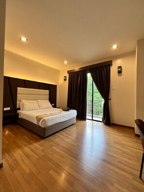 A bedroom with a large bed, a nightstand, a desk, and a view of greenery through the window. - HOTEL GRAND BARON TAIPNG (TAIPING)