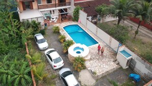 Una casa con piscina, un área de estar cubierta al aire libre y un camino de entrada pavimentado con coches estacionados.