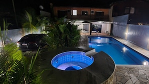 Una piscina con hidromasaje, rodeada por un patio de piedra y palmeras.