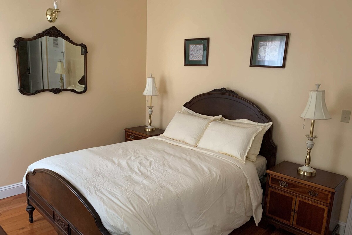 A bedroom with a wooden bed, two bedside tables, a mirror, and two framed pictures on the wall.