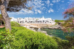 Uma vila costeira com edifícios brancos, céu azul límpido e costa rochosa.