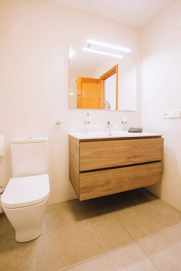 Un baño con inodoro blanco, tocador de madera y espejo sobre el lavabo.
