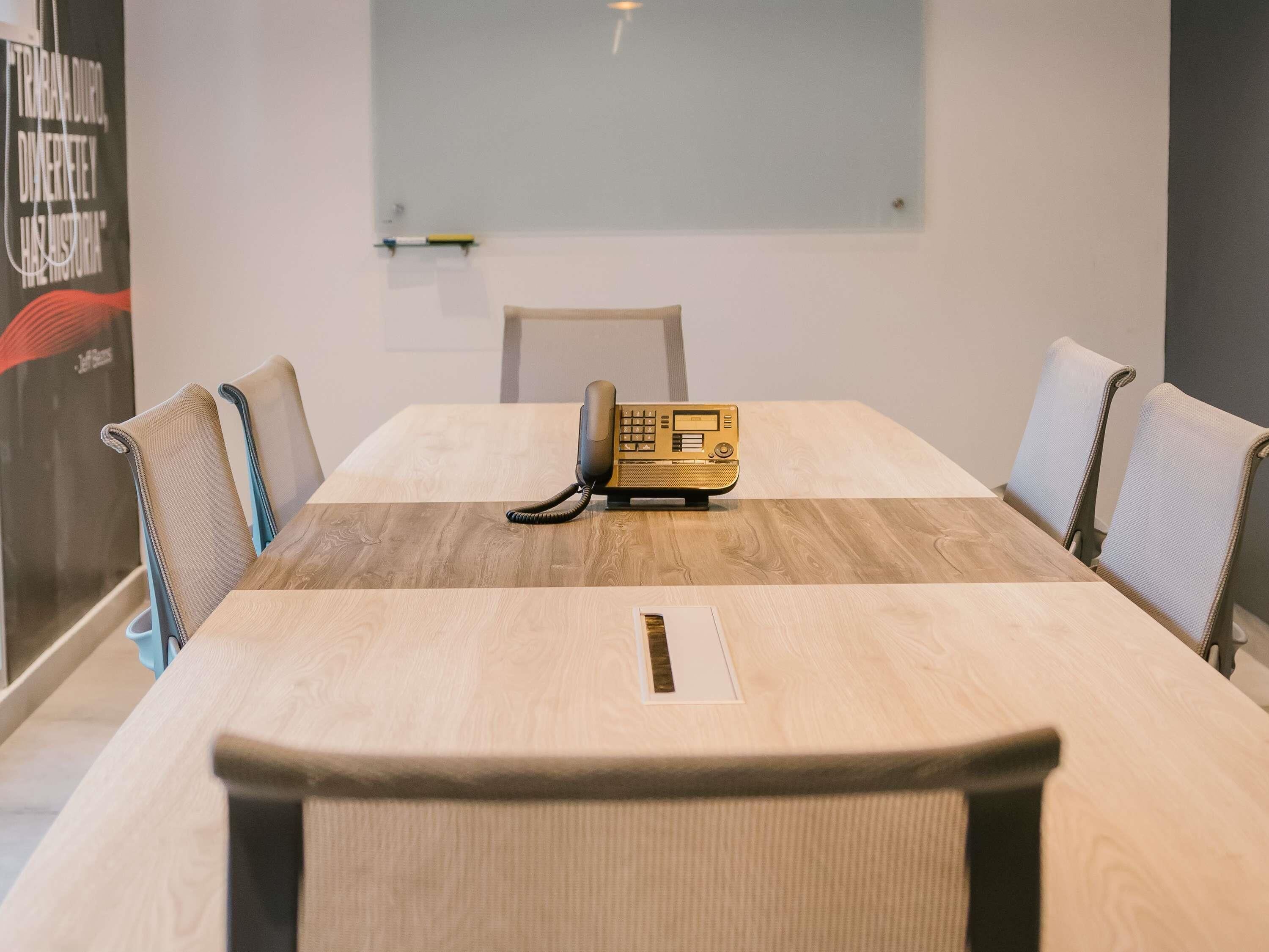 Una sala conferenze con un tavolo di legno, quattro sedie, un telefono d'epoca e un poster appeso al muro.