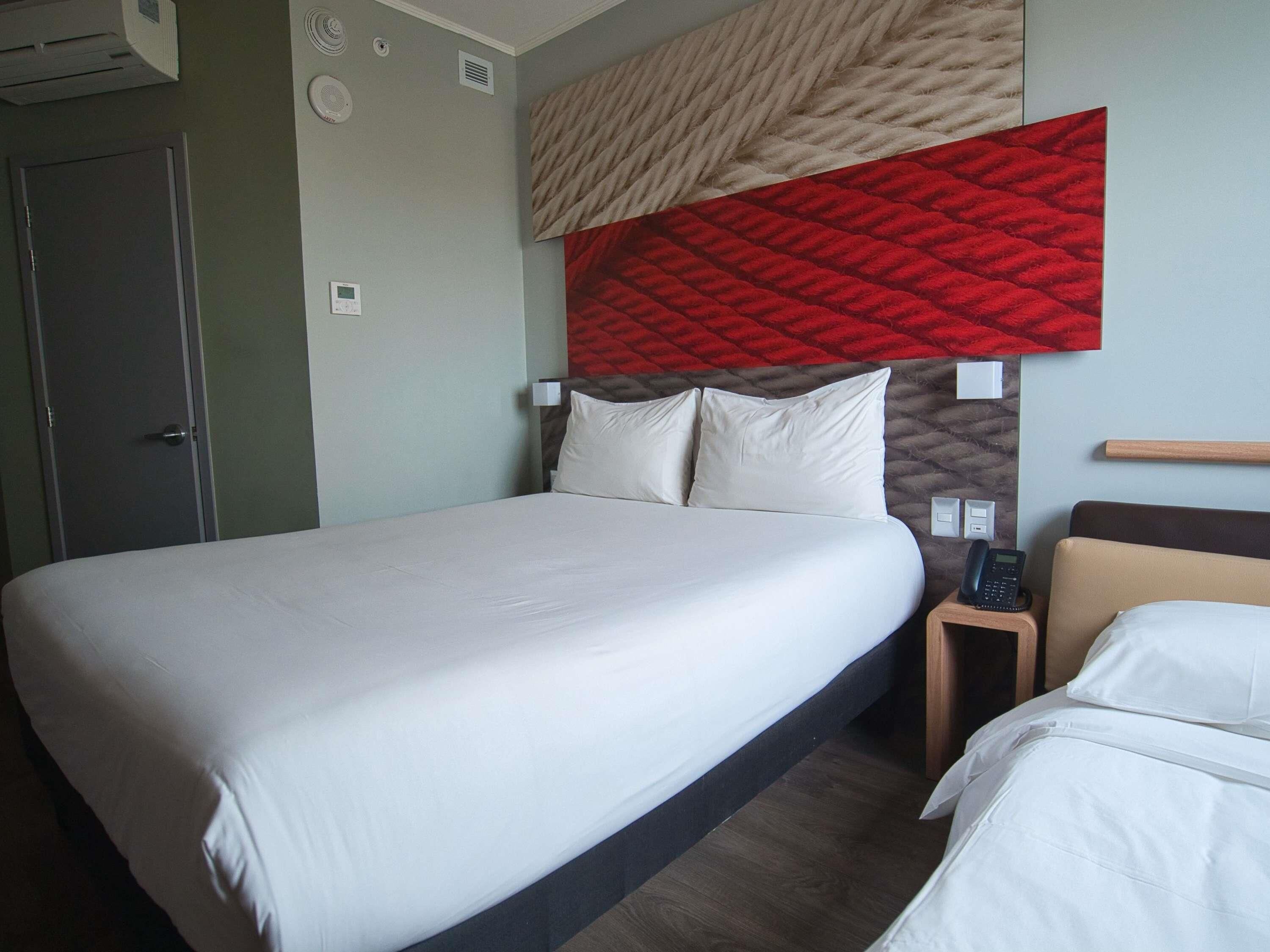 A hotel room with a large bed, bedside tables, a telephone, and a wall-mounted light switch.