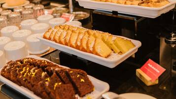Een buffet met diverse desserts, waaronder een brood, een schaal taarten en een chocoladetaart.