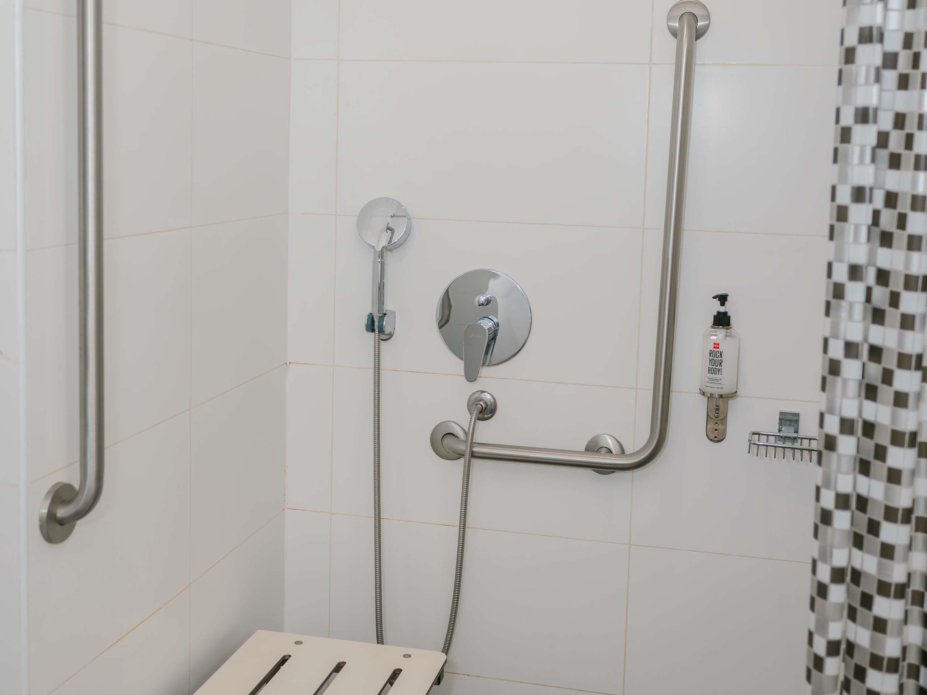 A shower area with grab bars, a handheld showerhead, and a soap dispenser.