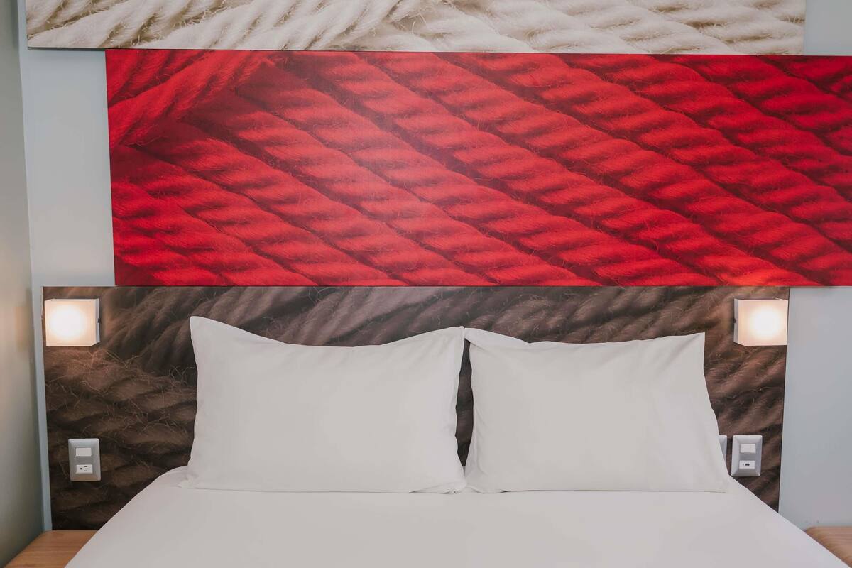 A bed with white linens, two bedside lamps, and a textured wall above.