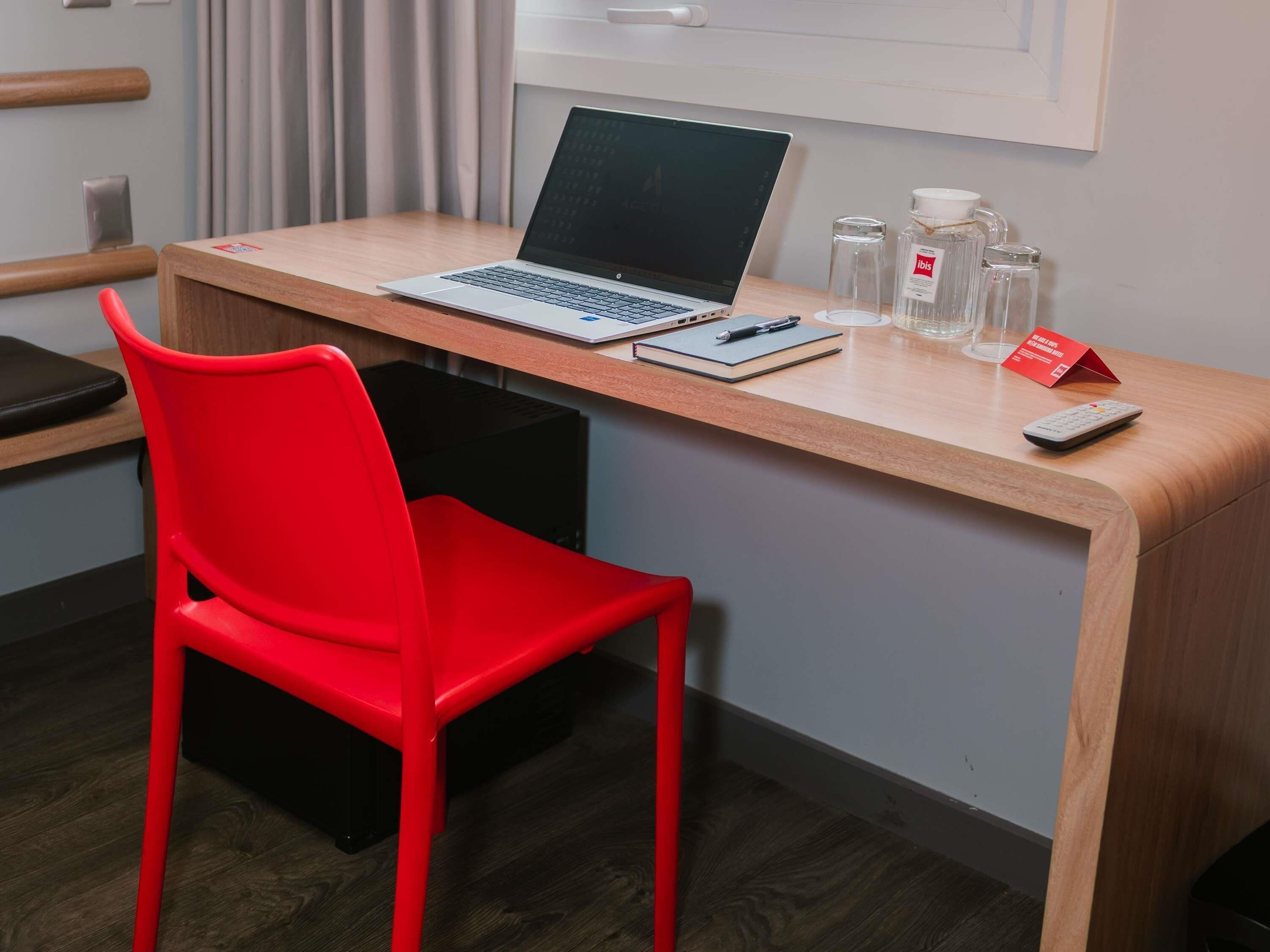 Espacio de trabajo en un hotel con una computadora portátil, libreta, bolígrafo y control remoto sobre un escritorio de madera.